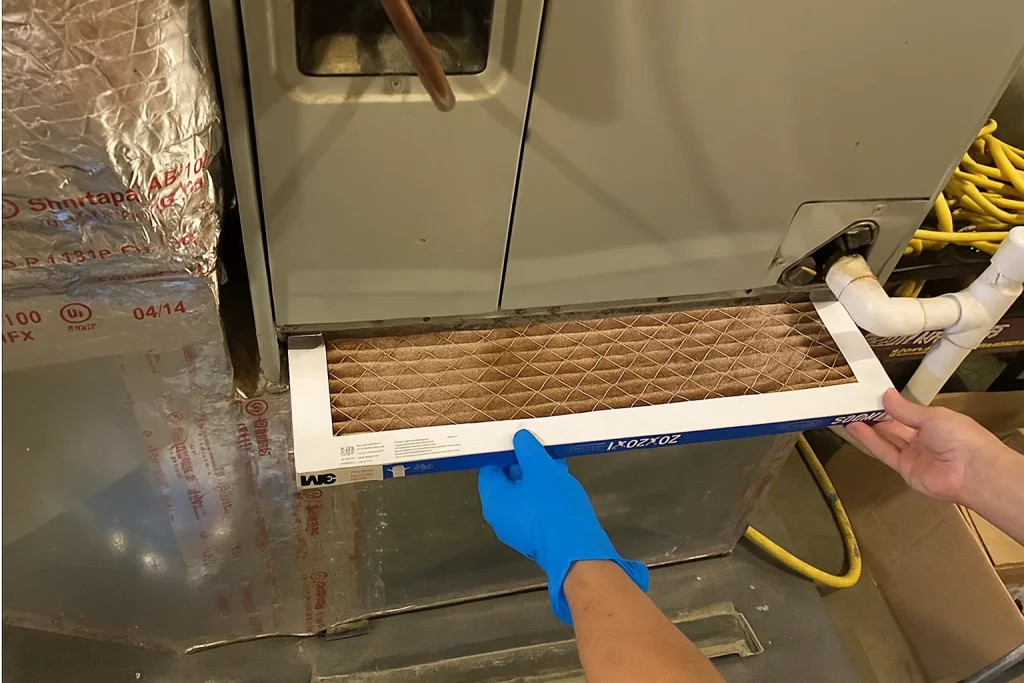 Close-up of dirty filter replacement and wiring checks in furnace after heavy summer use.