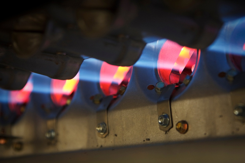 Close-up of a furnace burner with blue flames, emphasizing heating and air conditioning repair needs.