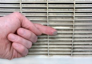 Finger showing heavy dust buildup on a dirty air purifier vent grille.